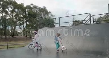 一个小男孩在滑板车上溜冰，女孩骑自行车在滑板坡道上半管